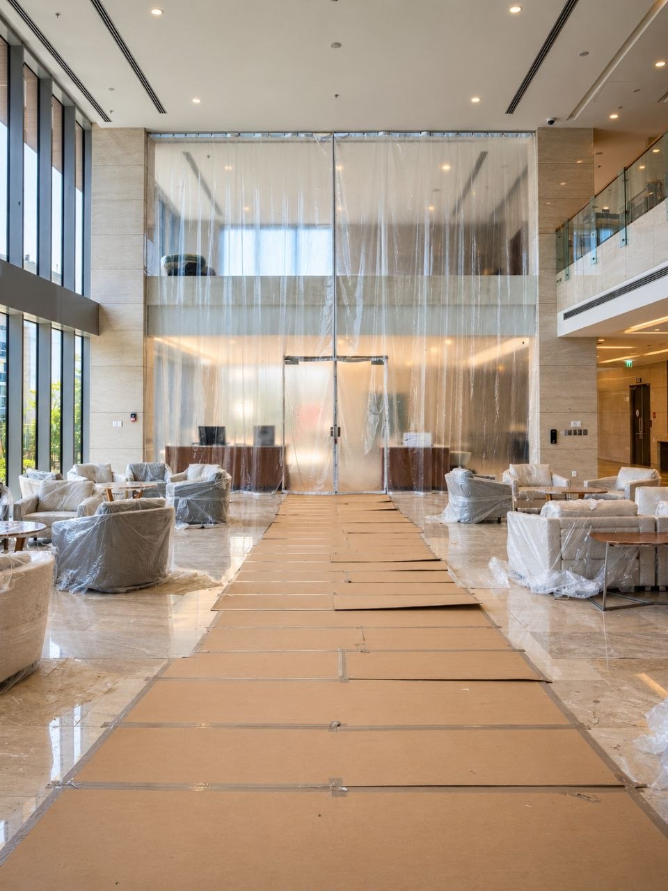 A hospital lobby prepared for work: seating under protective sheeting, floor boarded and taped, a containment curtain closing off the far end