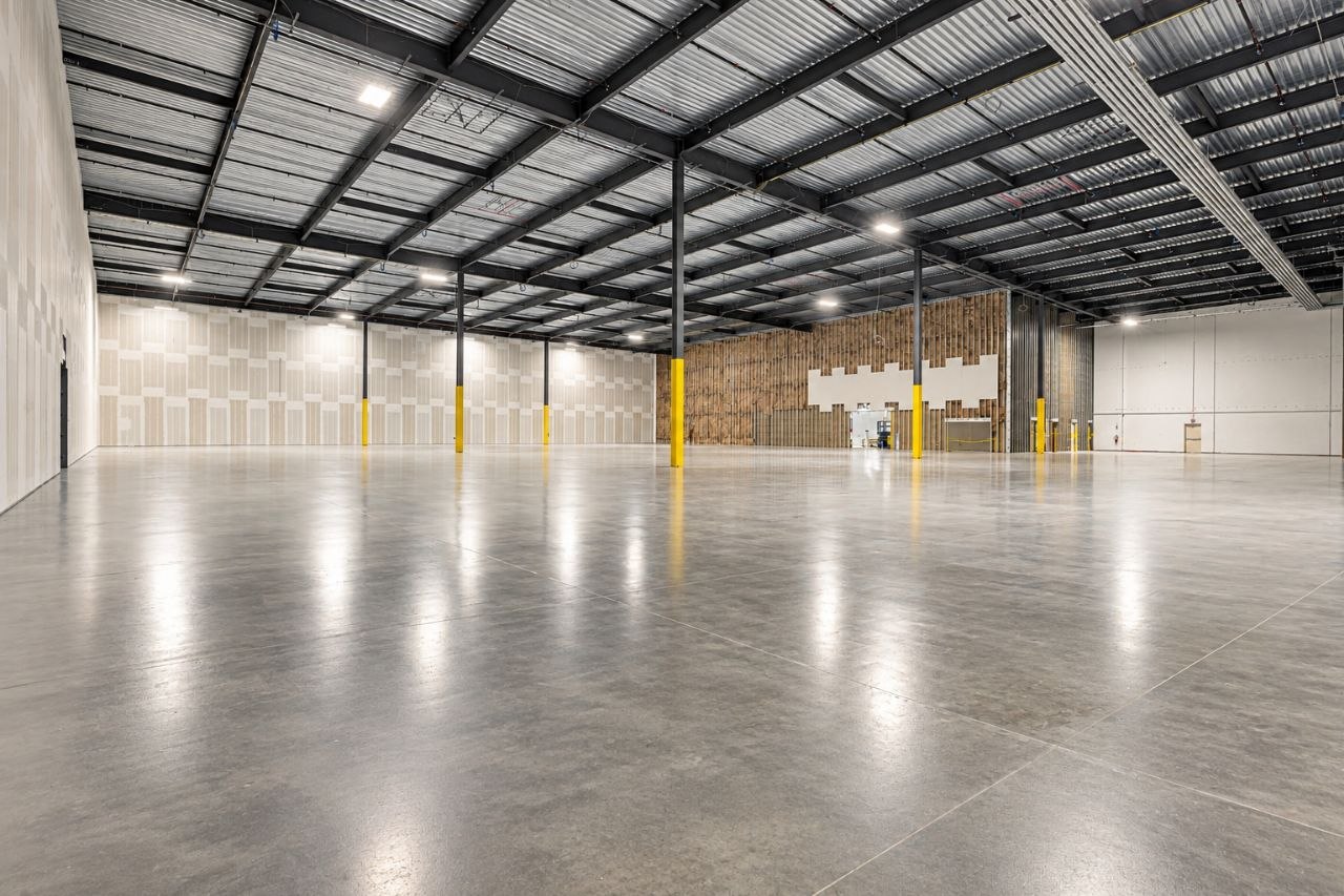 Interior of a newly built commercial building before fit-out: steel frame and deck overhead, painted walls, a sealed slab