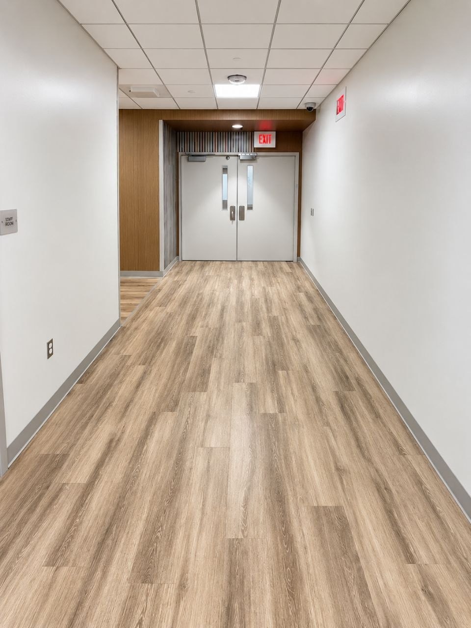 Completed corridor: plank floor run out straight, painted walls, ceiling grid and double doors at the far end